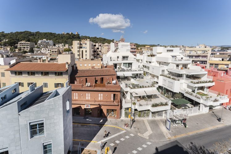 The project seen from a nearby rooftop, the blue, red, and white buildings clearly visible under a rich blue sky on a sunny day
